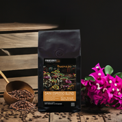 A bag of Buenaso Dark Espresso Blend coffee with a visual of coffee beans and a flower arrangement in the background.