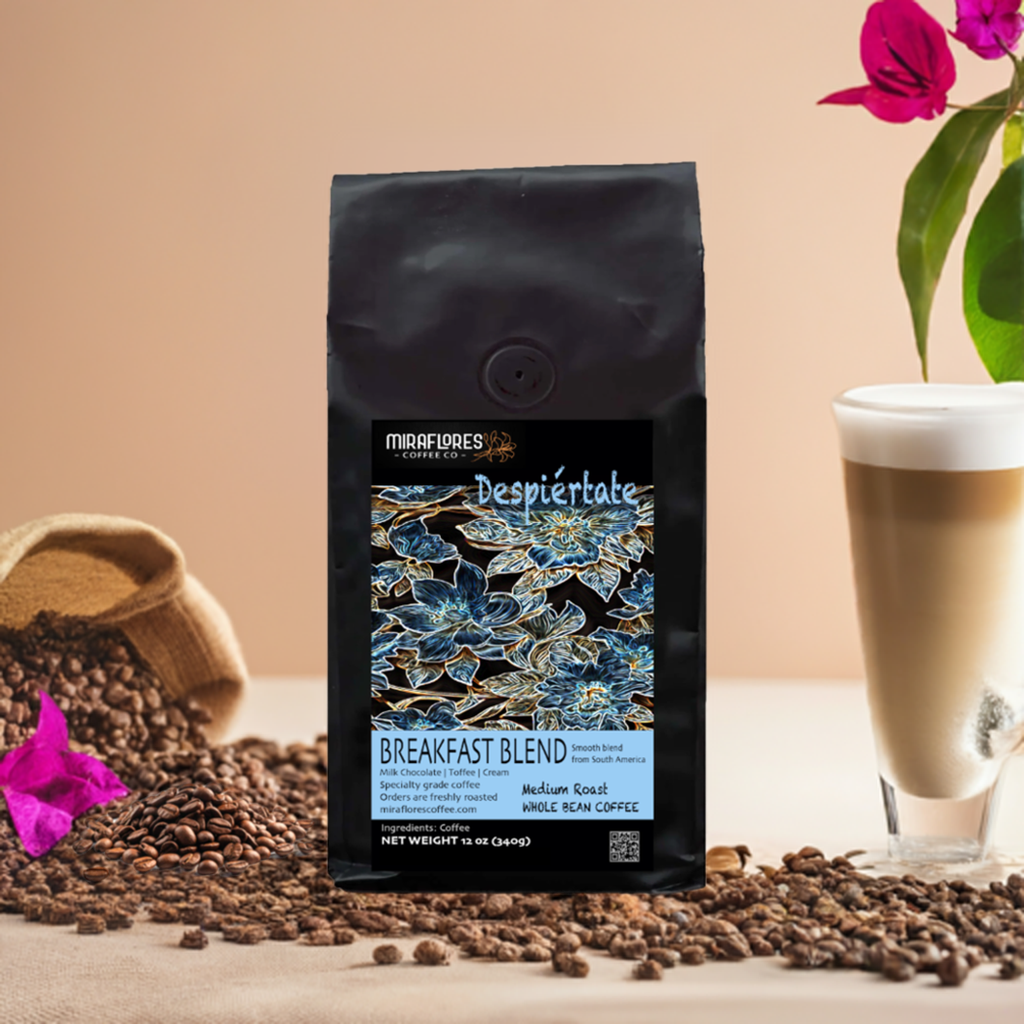 Bag of Despiertate Breakfast Blend coffee from Miraflores Coffee showing flavor notes of milk chocolate, caramel and cream, bag is set alongside roasted coffee beans, a tall glass of cappuccino and bright pink floers