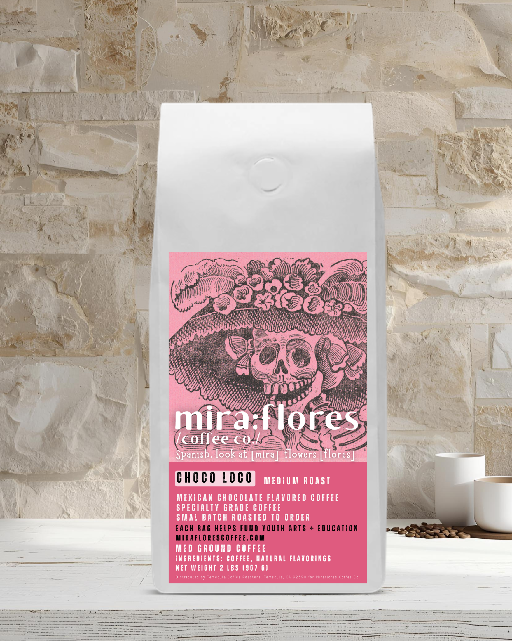 Specialty Coffee Beans bag of Mexican Chocolate flavored Coffee, Medium Roast, with pink design featuring a La Catrina by Jose Guadalupe Posada and Miraflores Coffee Co branding on a stone surface 