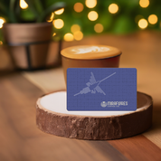 A blue gift card with an illustration of nazca lines and the Miraflores Coffee Co. logo, presented on a wood stum, resting on a cup of latte, there are decorative plants and lights in the background.