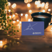 A purple gift card with an illustration of a nazca line and the Miraflores Coffee logo, presented on a table with a cup of coffee and decorative lights in the background.