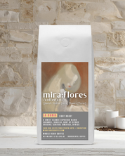 Specialty coffee bag for light roast medium roast sweet blonde espresso with miraflores branding and art masterpiece Girl with Blond Hair by Helene Schjerfbeck, set against a stone wall background